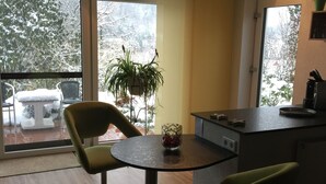 A modern kitchen with a round table and two chairs, a potted plant, and a view of a snowy outdoor area. - Apartment mit Burgblick im Grünen, Familie Held (Burgthann)
