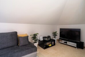 A modern living room with a grey sofa, a black entertainment unit, a flat-screen TV, and two potted plants. - Santa Luzia Funchal View | 2br pool, ac & parking (Funchal)