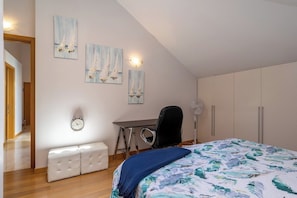 A bedroom with a bed, a desk, a chair, a bench, and artwork on the wall.
