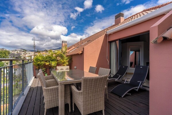A balcony with wicker furniture, a glass table, and lounge chairs. - Santa Luzia Funchal View | 2br pool, ac & parking (Funchal)