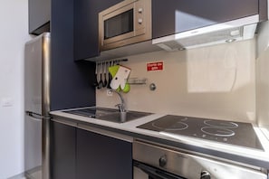 Cocina compacta con refrigerador de acero inoxidable, microondas y estufa.