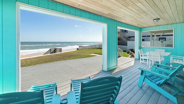 A beachside patio with a view of the ocean, outdoor seating, and a covered area with tables and chairs.