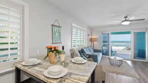 A dining area with a marble table set for four, a sofa, and a view of the ocean through large windows.