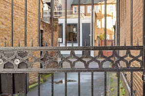 A metal gate with a decorative pattern, leading to a narrow alley with brick walls and a paved path.