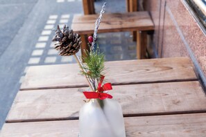 Una mesa de madera con un jarrón blanco que contiene una piña y una ramita de follaje atada con un lazo rojo.