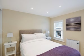 A bedroom with a bed, bedside tables, a window with blinds, a radiator, and a wall-mounted artwork.