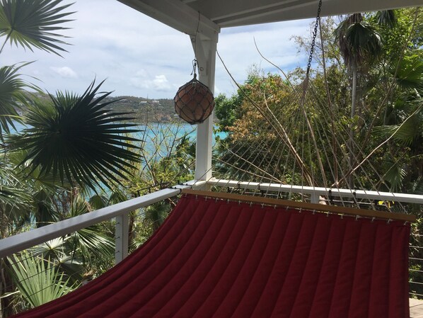 Een hangmat op een balkon met uitzicht op de zee en omliggende begroeiing.
