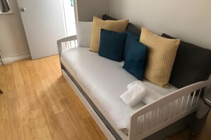 En enkeltseng med hvid madras, hvid sengegavl og et hvidt natbord med lampe.