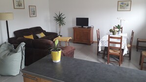 Ein Wohnzimmer mit einer Couch, einem Fernseher, einem Esstisch mit Stühlen und einer Topfpflanze.
