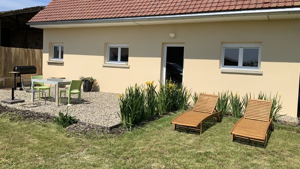 Ein Haus mit Ziegeldach, einer Terrasse mit Tisch und Stühlen sowie zwei Holzliegen.