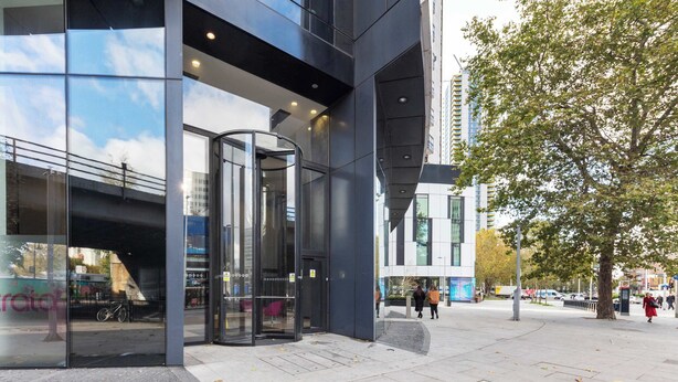 A modern building with large glass windows, a revolving door, and a paved sidewalk. - 1BD Flat with City Views, Elephant & Castle (London)