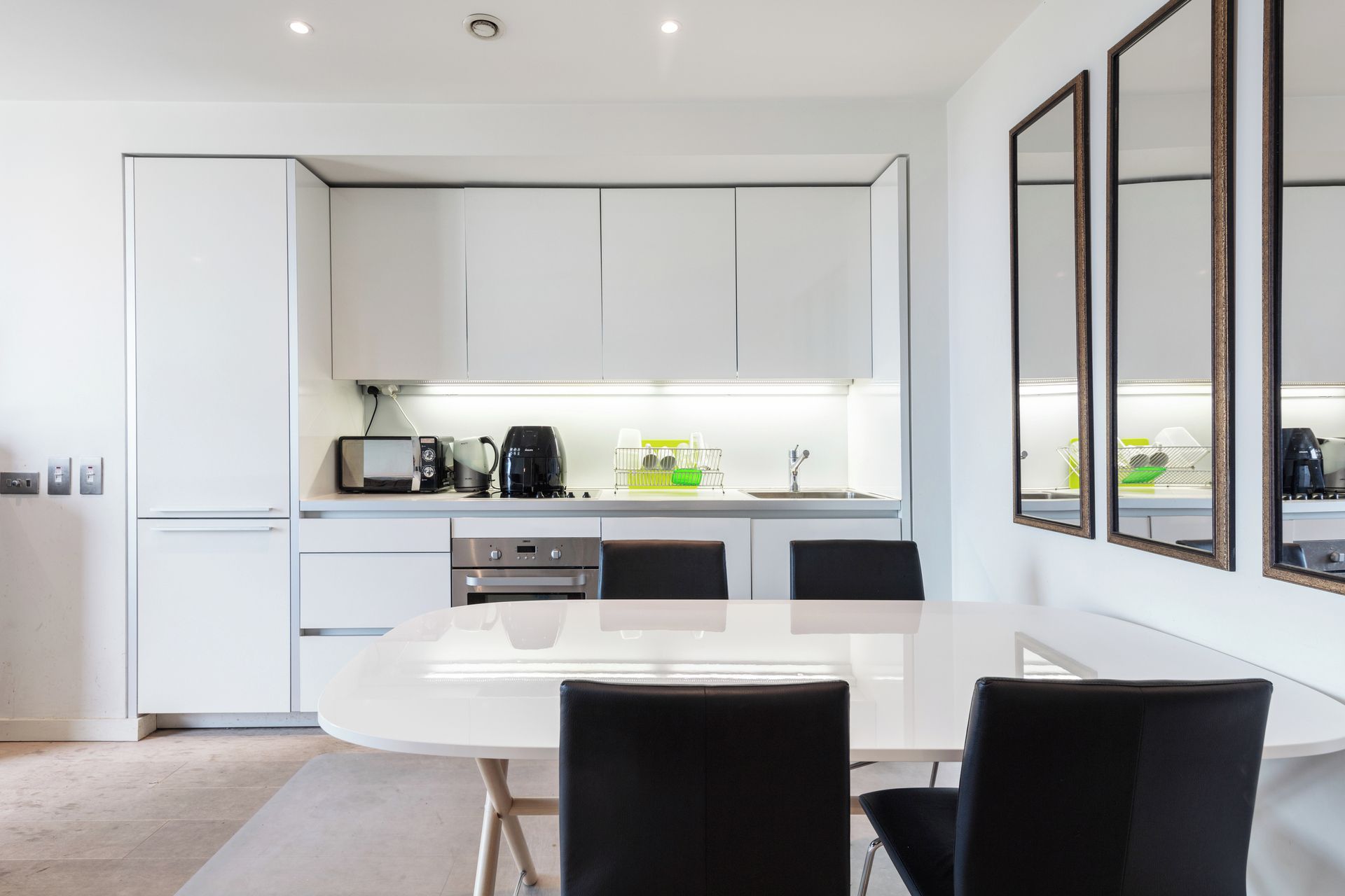 Une cuisine moderne avec des meubles blancs, une table à manger blanche et des chaises noires.