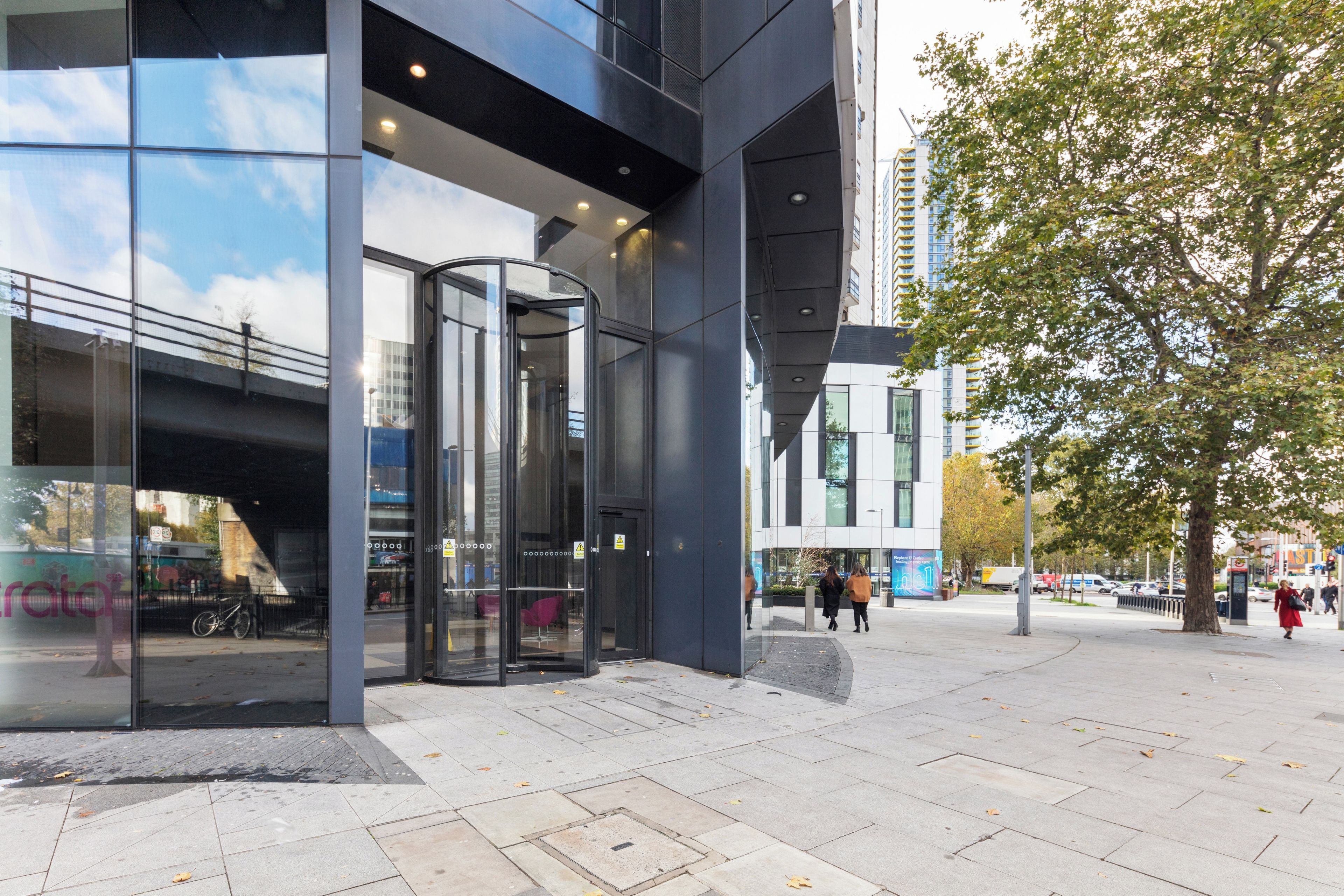 Un bâtiment moderne doté d’une façade en verre, d’une porte tournante à l’entrée et d’un passage piétonnier.