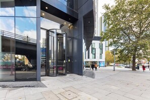 A modern building with a glass facade, a revolving door entrance, and a pedestrian walkway. - 1BD Flat with City Views, Elephant & Castle (London)