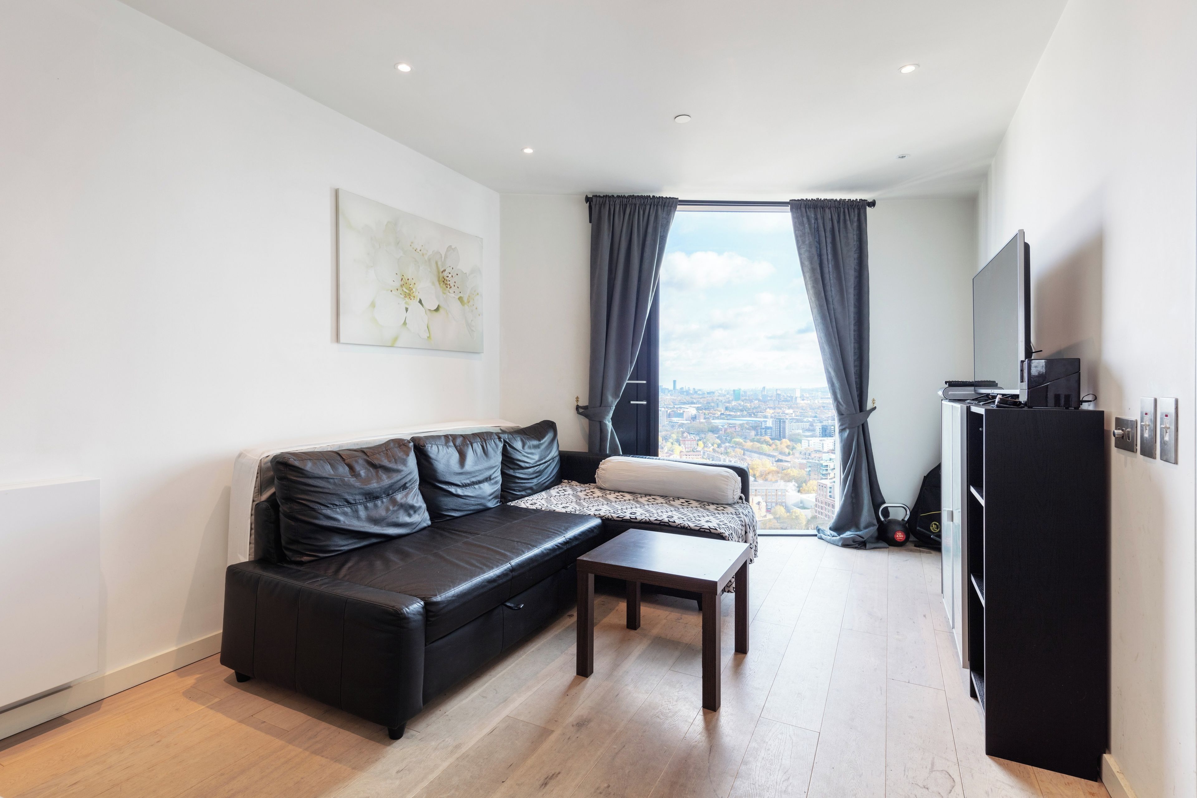 Un salon moderne avec un canapé en cuir noir, une petite table basse et une vue sur la ville grâce à de grandes fenêtres.