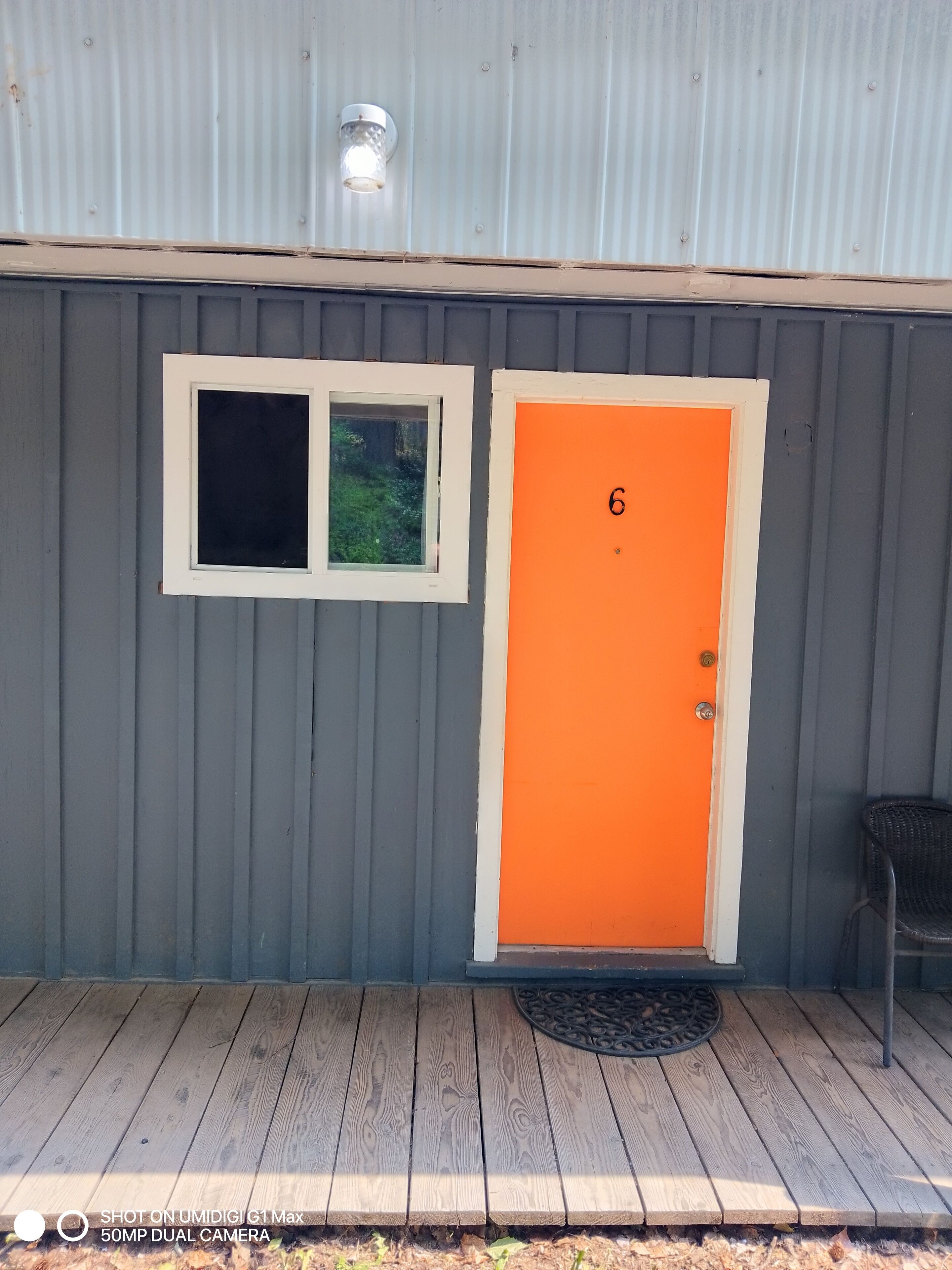 Un edificio gris con un marco blanco en la ventana y una puerta naranja con el número 6.