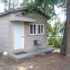 A small cabin with a door, a window, and a chair outside.