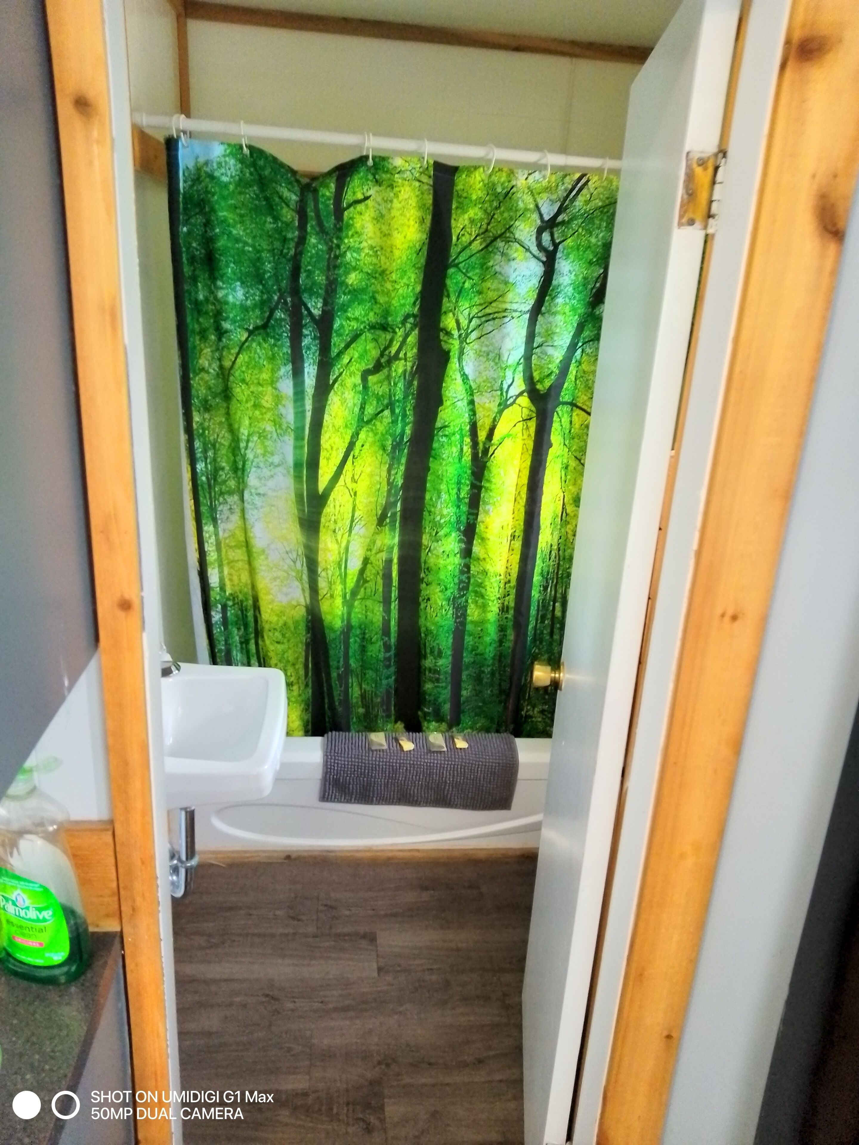 A bathroom with a forest-themed shower curtain, a white sink, and a bench.