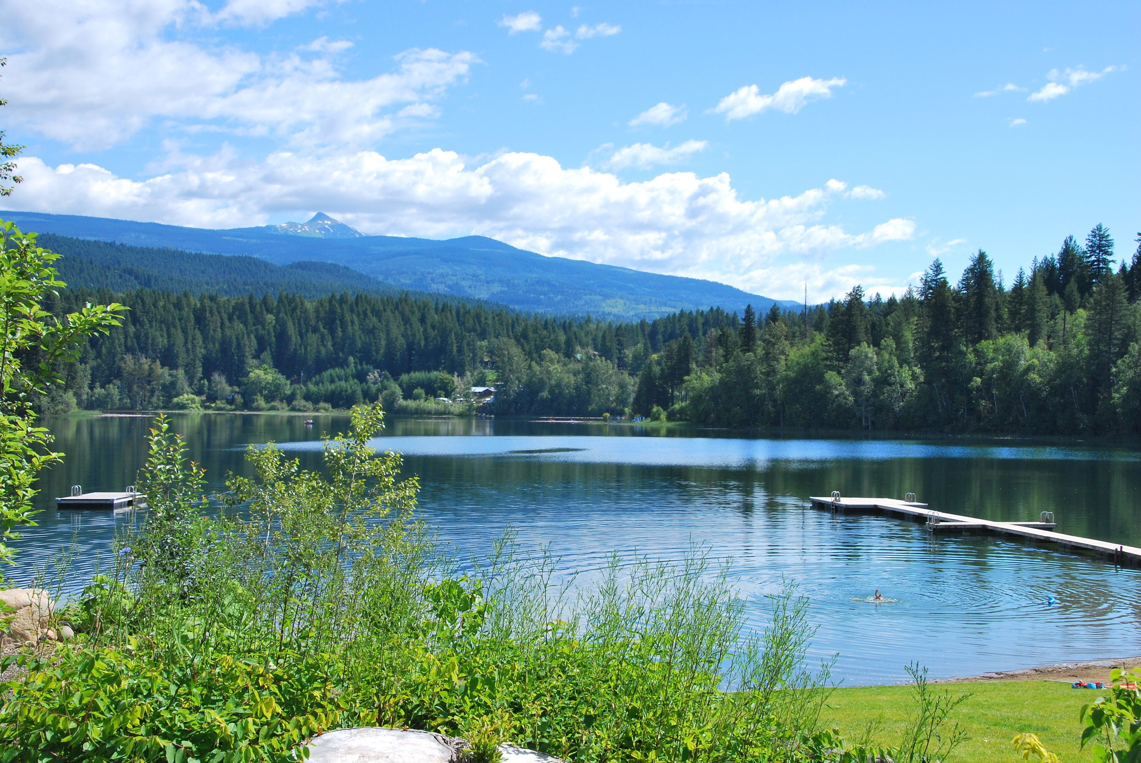 A serene lake with docked boats, surrounded by lush greenery and distant mountains.