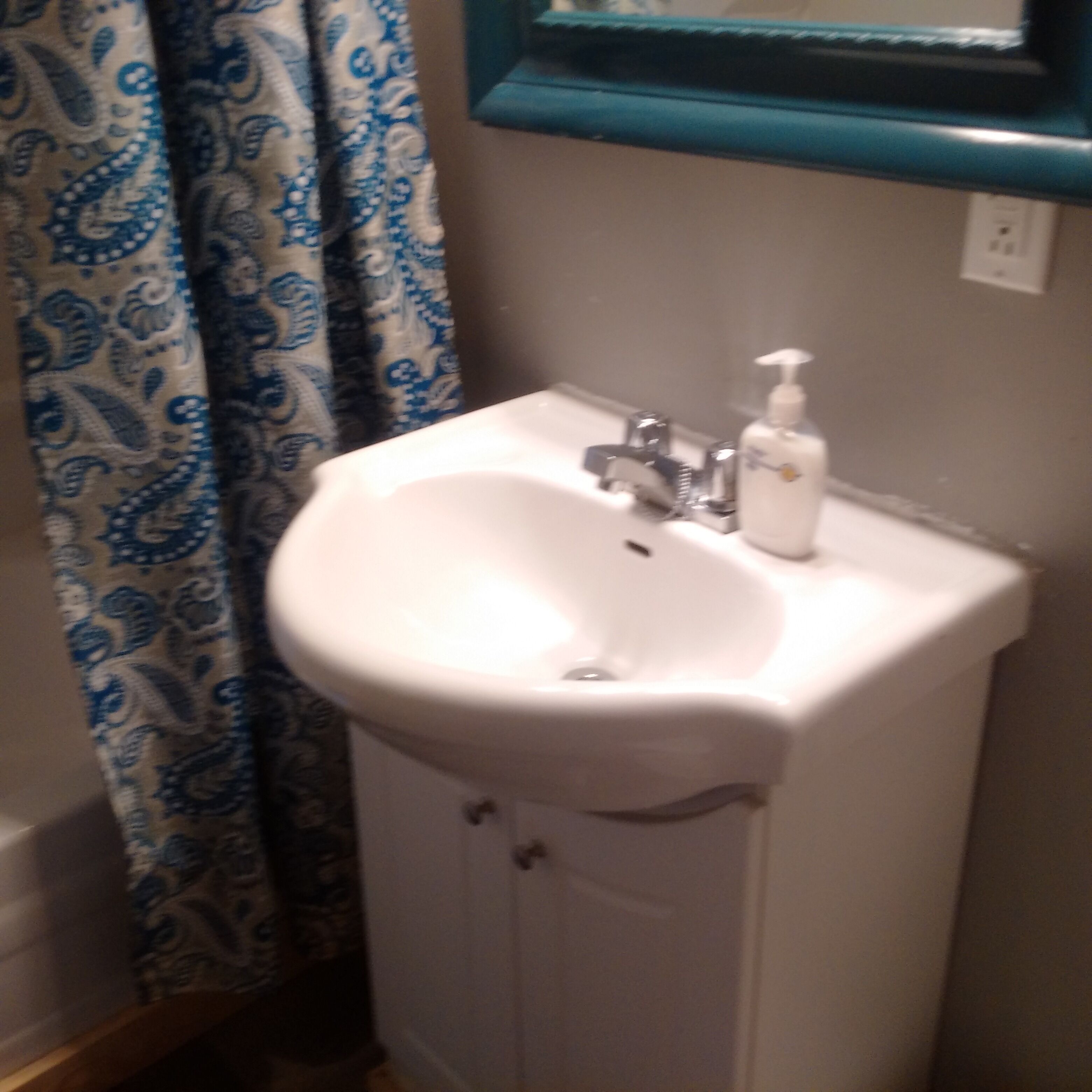 A bathroom with a white sink, a mirror above it, and a blue and white patterned shower curtain.