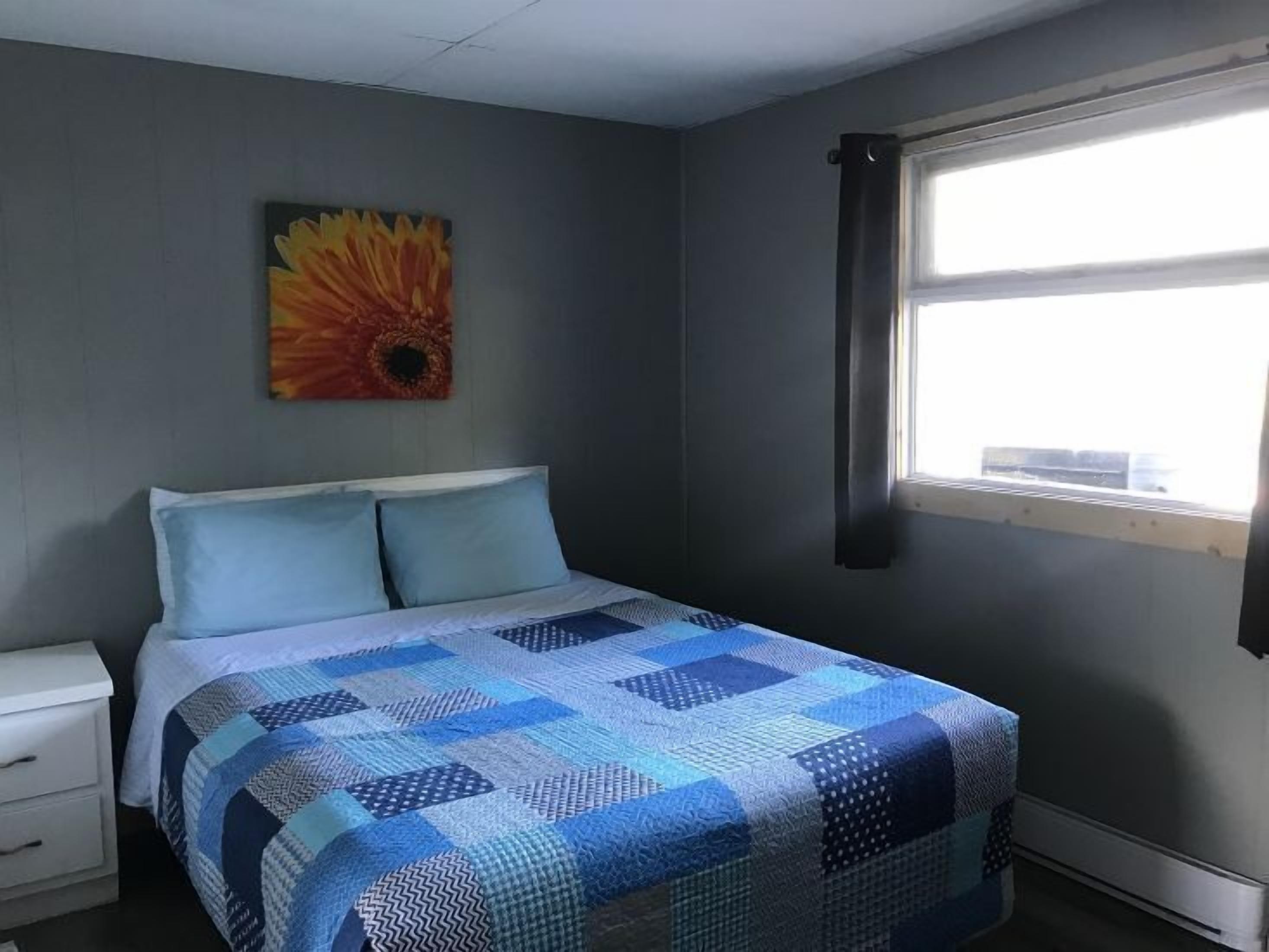 A bedroom with a bed, a nightstand, a window with curtains, and a painting on the wall.
