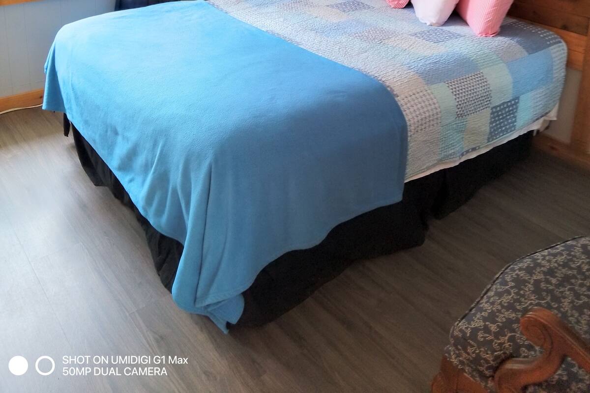 Un dormitorio con cama, mesita de noche, lámpara, ventana con cortinas y un cuadro en la pared.