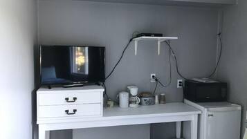 Un escritorio pequeño y blanco con televisión, cafetera, microondas y refrigerador pequeño.