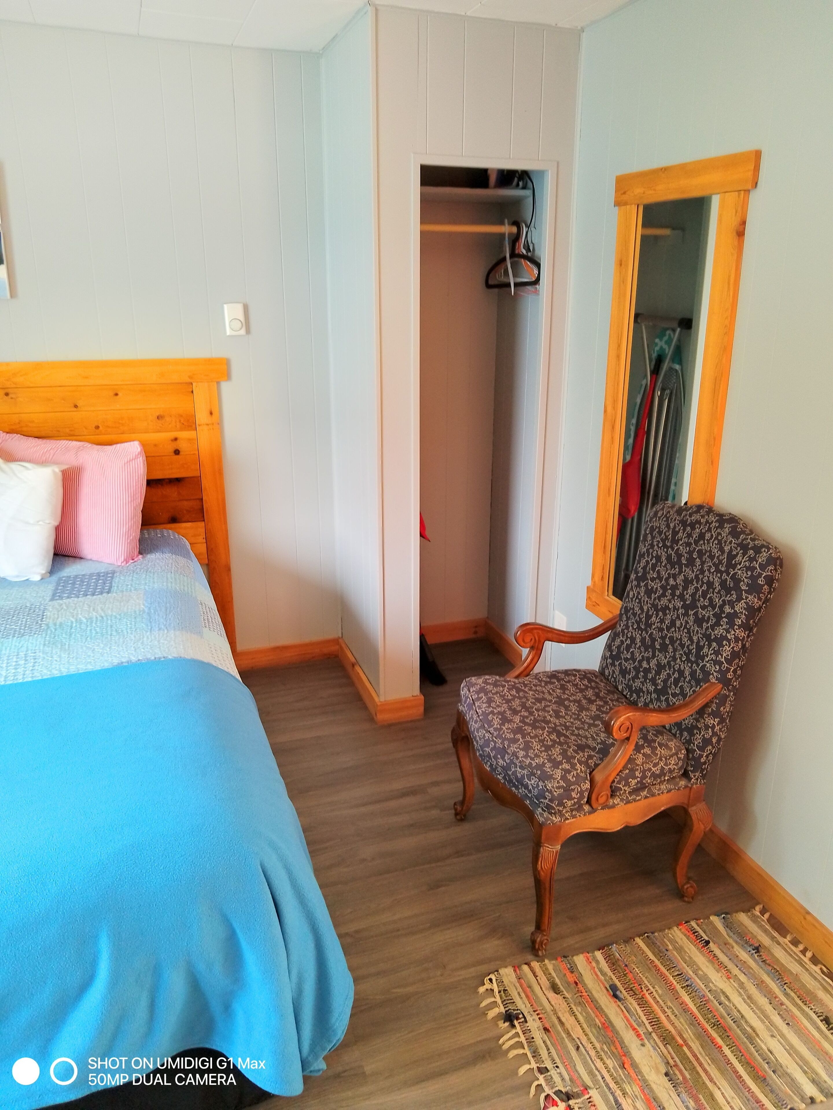 A bedroom with a wooden bed, a patterned armchair, a striped rug, and a wardrobe.