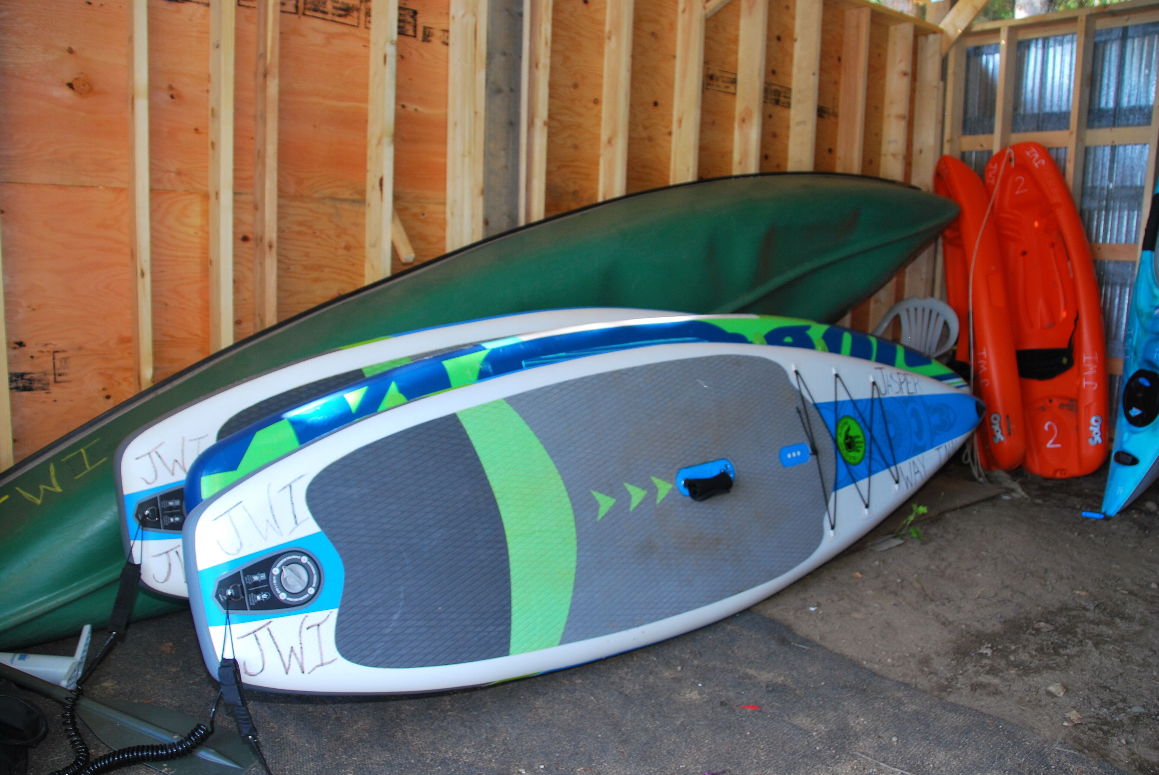 Una habitación con paredes de madera y suelo de concreto, que contiene varias kayaks y una tabla de surf.