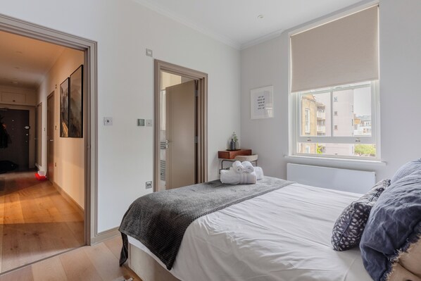 A bedroom with a bed, a window, and a door leading to another room.