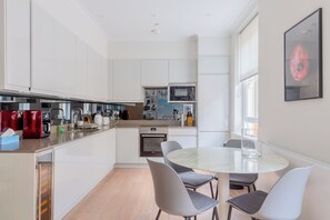 Eine moderne Küche mit weißen Schränken, einem eingebauten Backofen und einem Essbereich mit rundem Tisch und Stühlen.