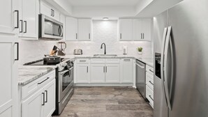 A modern kitchen with white cabinetry, stainless steel appliances, and a marble countertop. - Chefs Kitchen, King Beds, Smart TVs. Close to downtown! Dead End Street (Greenville)