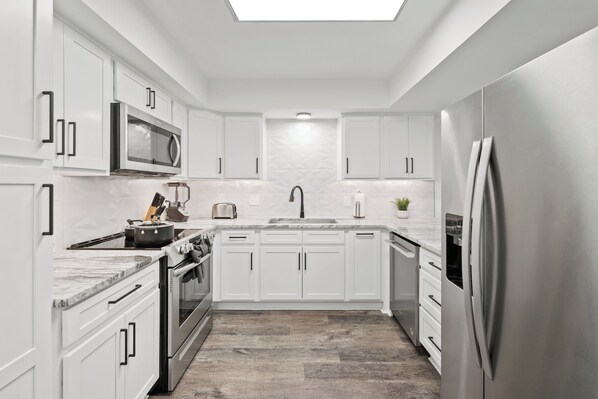 A modern kitchen with white cabinetry, stainless steel appliances, and a marble countertop.