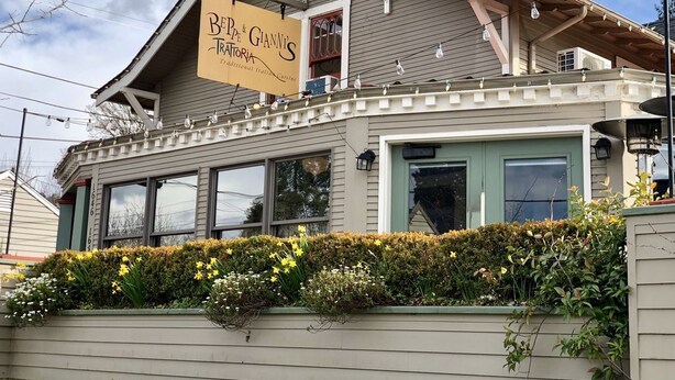 Ein traditionelles italienisches Restaurant mit Schild, großen Fenstern und einem gepflegten Garten.