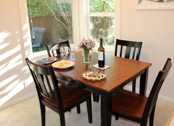 Une table à manger avec quatre chaises, une bouteille de vin, un vase de fleurs et des assiettes remplies de nourriture.