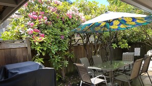 Eine Terrasse im Freien mit einem Glastisch, Stühlen, einem schattenspendenden Sonnenschirm und einem Holzzaun.