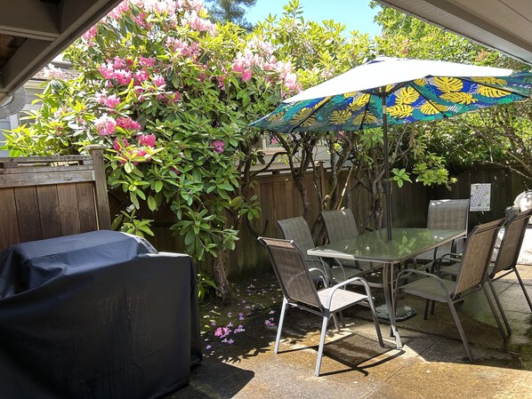 Une terrasse extérieure avec une table et des chaises en verre, un parasol et une clôture en bois.