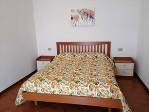 Une chambre à coucher avec un lit en bois, une couvre-lit à motifs floraux, deux tables de chevet et un tableau accroché au mur.