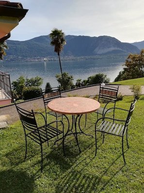 Une terrasse avec une table ronde et quatre chaises, offrant une vue sur un lac et des montagnes.