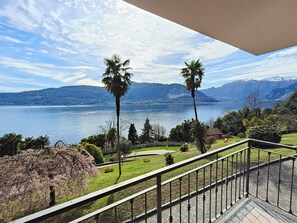 Un balcon avec vue sur un lac, des montagnes et un jardin agrémenté de palmiers.