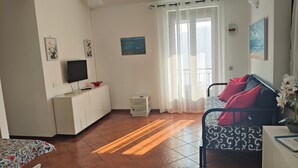Une pièce bien éclairée, avec un lit, une télévision, une petite table et une fenêtre avec des rideaux.