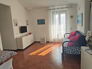 Une pièce bien éclairée, avec un lit, une télévision, une petite table et une fenêtre avec des rideaux.