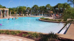 Una piscina con fuentes, palmeras y sillas de descanso.