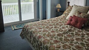 Un dormitorio con cama, ventilador de techo, ventana con persianas y vista al exterior.