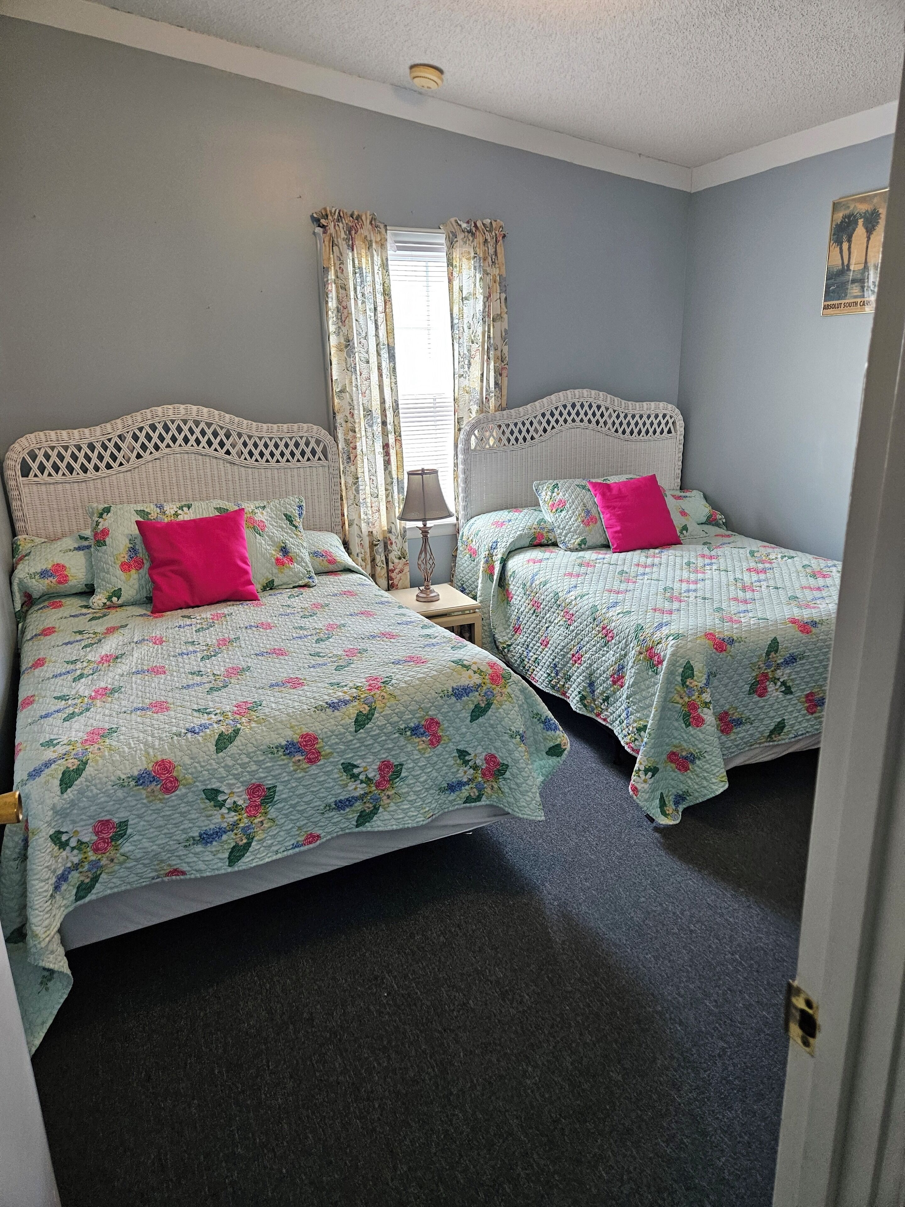 Une chambre avec deux lits, une literie à motifs floraux et une fenêtre avec des rideaux.