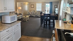 Una cocina con pisos de madera, armarios blancos, microondas y un comedor con mesa y sillas.