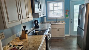 Una cocina con armarios blancos, encimera de granito, electrodomésticos de acero inoxidable y una ventana con persianas.