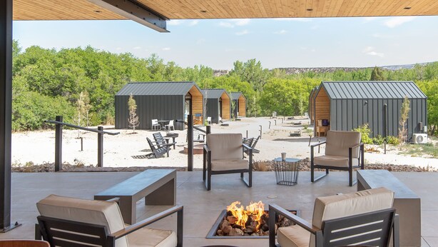 Un patio al aire libre con mobiliario de madera, una fogata y vistas del paisaje circundante.
