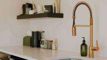A kitchen with a white countertop, a stainless steel sink, and a gold faucet.