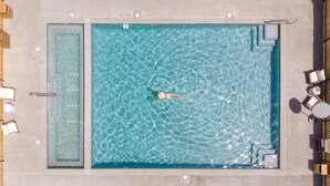 Vista aérea de una piscina rectangular con agua azul cristalina, rodeada de sillas y mesas de descanso.